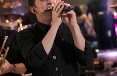 Man in black shirt singing into a microphone on stage.