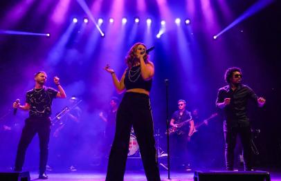 Band performing on stage under bright purple lights.