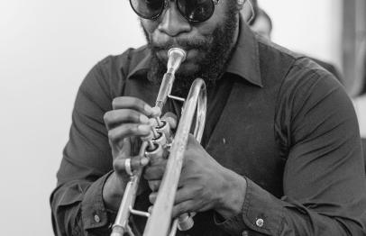 Man wearing sunglasses playing trumpet indoors, black and white photo.