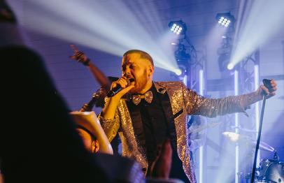 Singer in a sparkling jacket performing on stage with dramatic lighting.