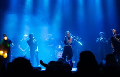 Band performing on stage under blue lights with an audience in the foreground.