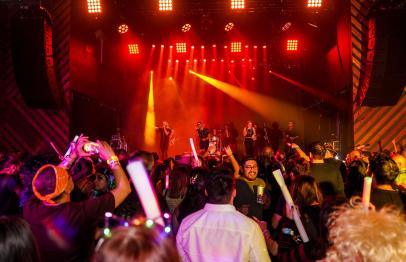 Crowd enjoying a concert with bright stage lights and performers in the background.