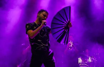 Singer holding a fan performs on stage under purple lights.