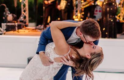 Groom dipping bride for a kiss on the dance floor, band playing in the background.