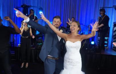 Bride and groom joyfully dancing at a wedding reception with blue stage lights.
