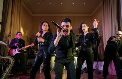 Band performing energetically on stage with lead singer in foreground.