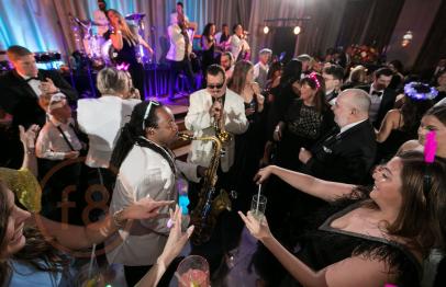 Crowd dancing and celebrating around a saxophone player at a lively indoor party.