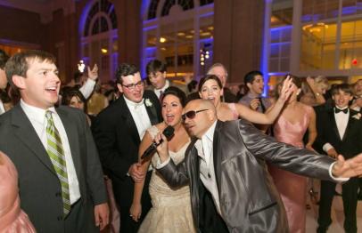 People dancing and singing at a formal wedding reception with lively expressions.