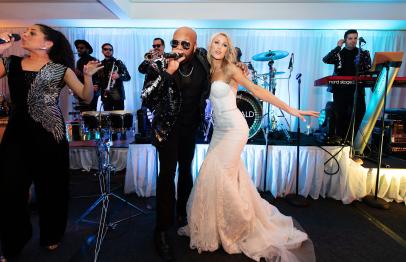 Bride in white dress dancing and singing with a live band at a wedding reception.