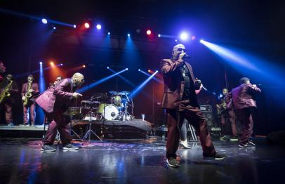 Band performing energetically on stage under colorful lights.