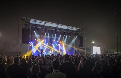 Crowd watching a concert at night with colorful stage lights and large screens.