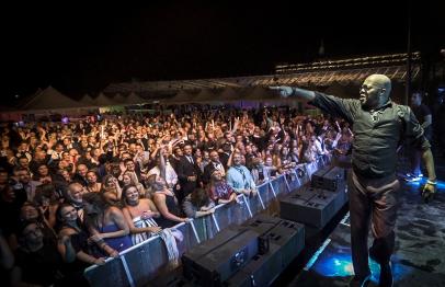 Singer on stage pointing at a cheering crowd during a nighttime outdoor concert.