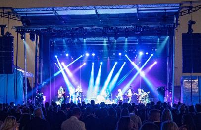 Outdoor concert stage with colorful lights and a crowd watching the performance.