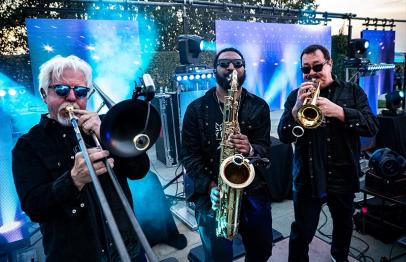 Three musicians playing brass instruments on an outdoor stage at sunset.