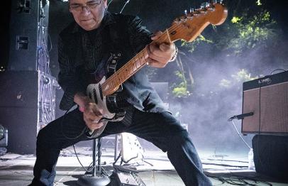 Guitarist playing energetically on stage with dramatic lighting and smoke.