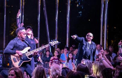 Band performing on stage at night with cheering crowd and colorful lights.