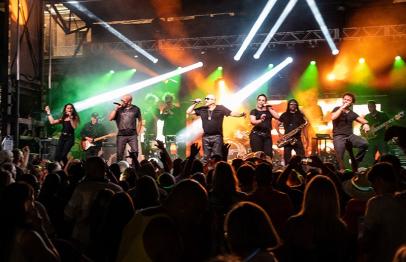 Band performing on stage with colorful lights and a cheering crowd at night.