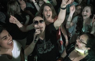 Singer with microphone surrounded by excited crowd at a concert.