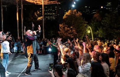 Musicians performing on an outdoor stage at night for a cheering crowd.
