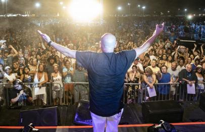 Performer on stage facing a large, cheering crowd at night with bright lights behind.
