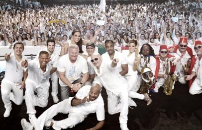 Performers in white pose on stage with a cheering crowd in the background.