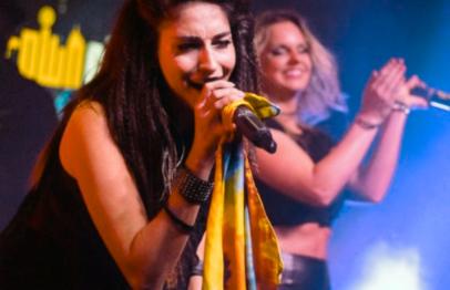 Woman singing on stage with a microphone, another woman clapping behind her.
