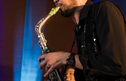 Man in sunglasses playing saxophone on stage with colorful lighting.