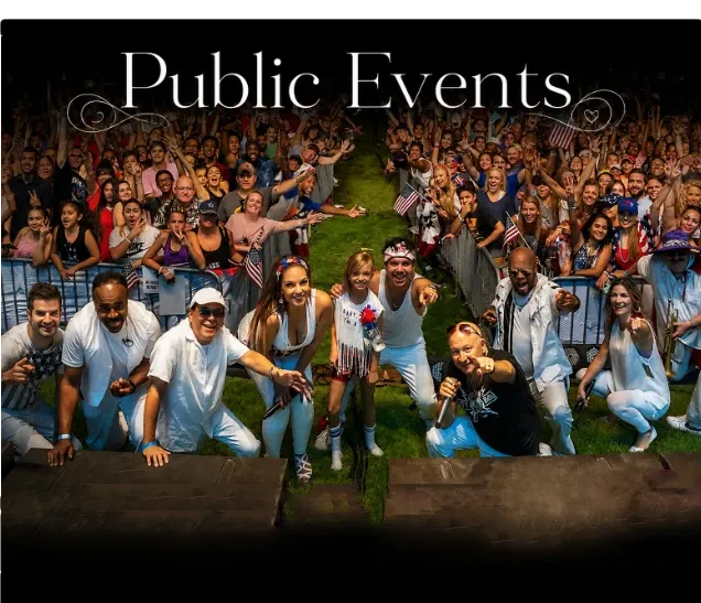 Performers in white pose on stage with a cheering crowd behind them at an outdoor event.