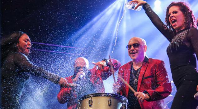Close up of Deno and three band members performing under the spotlight