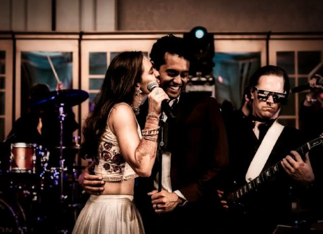Woman singing to smiling man on stage with a guitarist and drummer in the background.