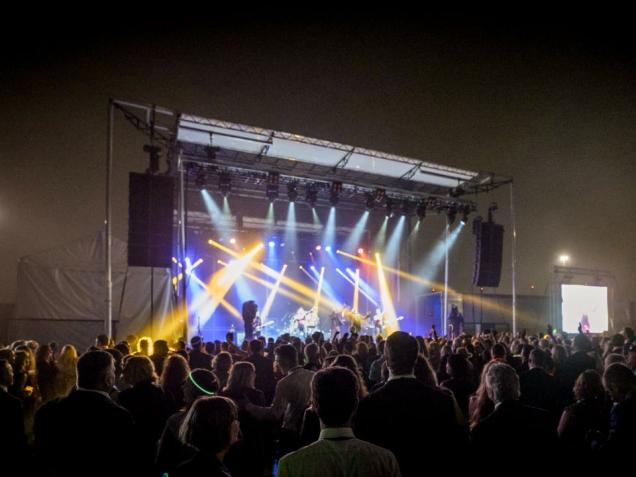 Crowd watching a concert on an outdoor stage with colorful lights at night.
