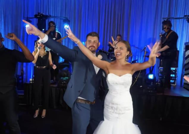 Bride and groom dancing joyfully at a lively wedding reception with blue lighting.