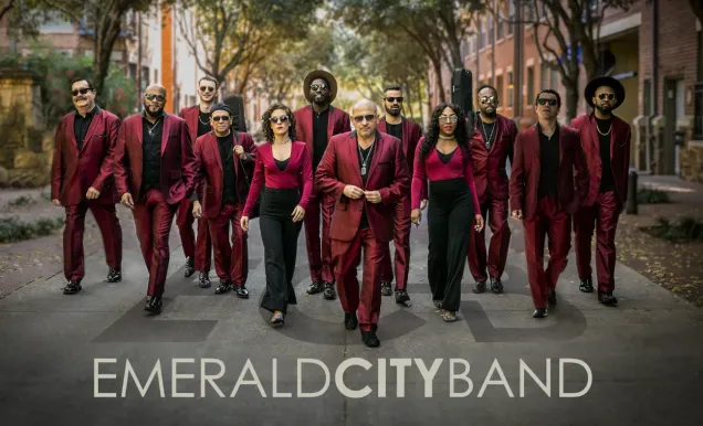 A group of people in matching red suits walking confidently down a tree-lined street.