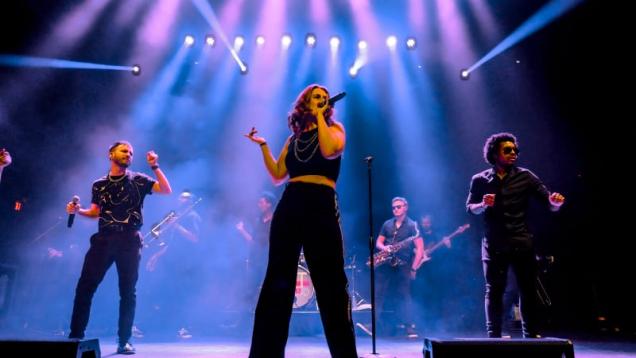 Band performing on stage under colorful lights with a female lead singer.