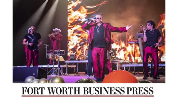 Band in red suits performing onstage with fire graphics in the background.