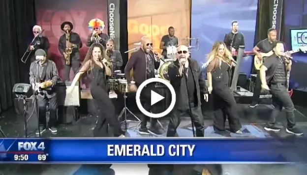 Band performing live on a news studio stage with "Emerald City" text on screen.