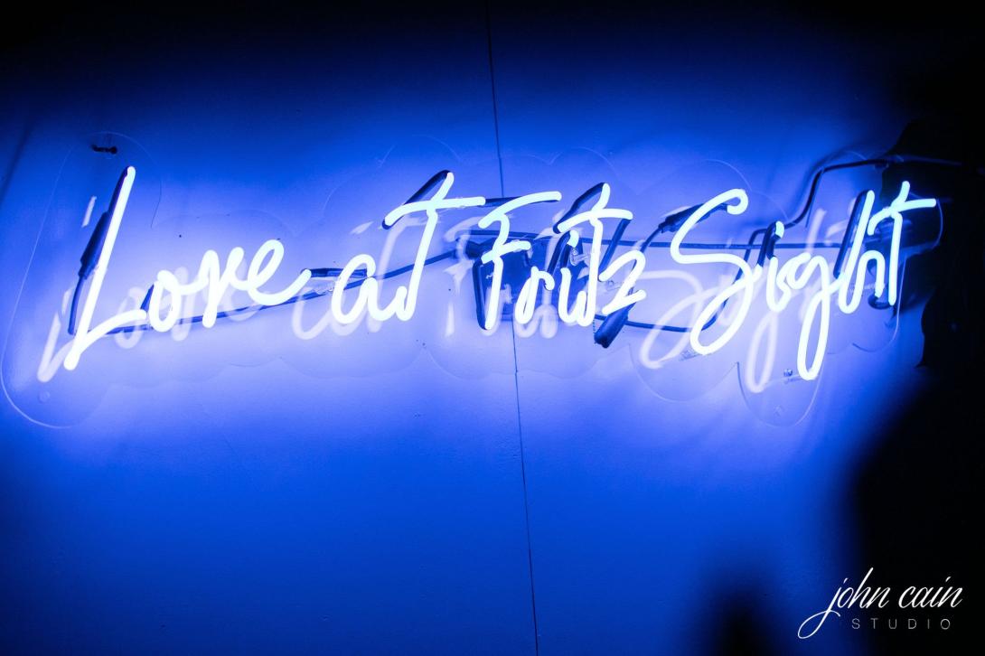 Blue neon sign reads "Love at First Sight" against a dark background.