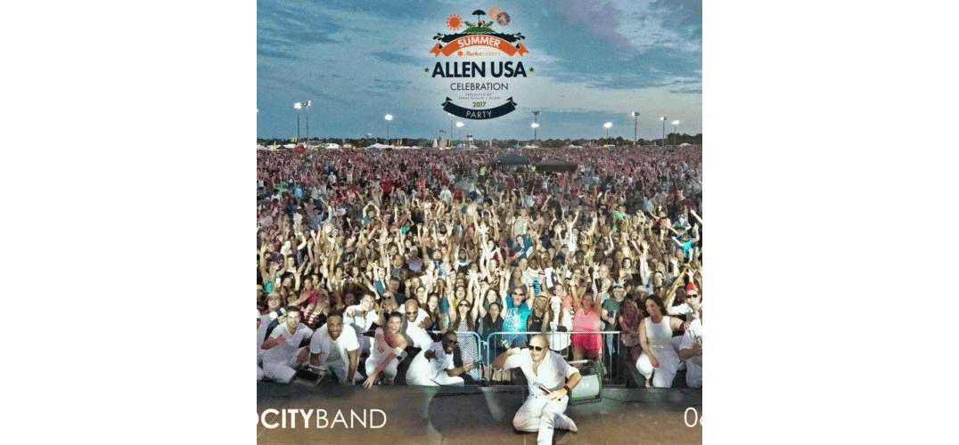Large outdoor crowd at a festival, with musicians in white uniforms posing in front.