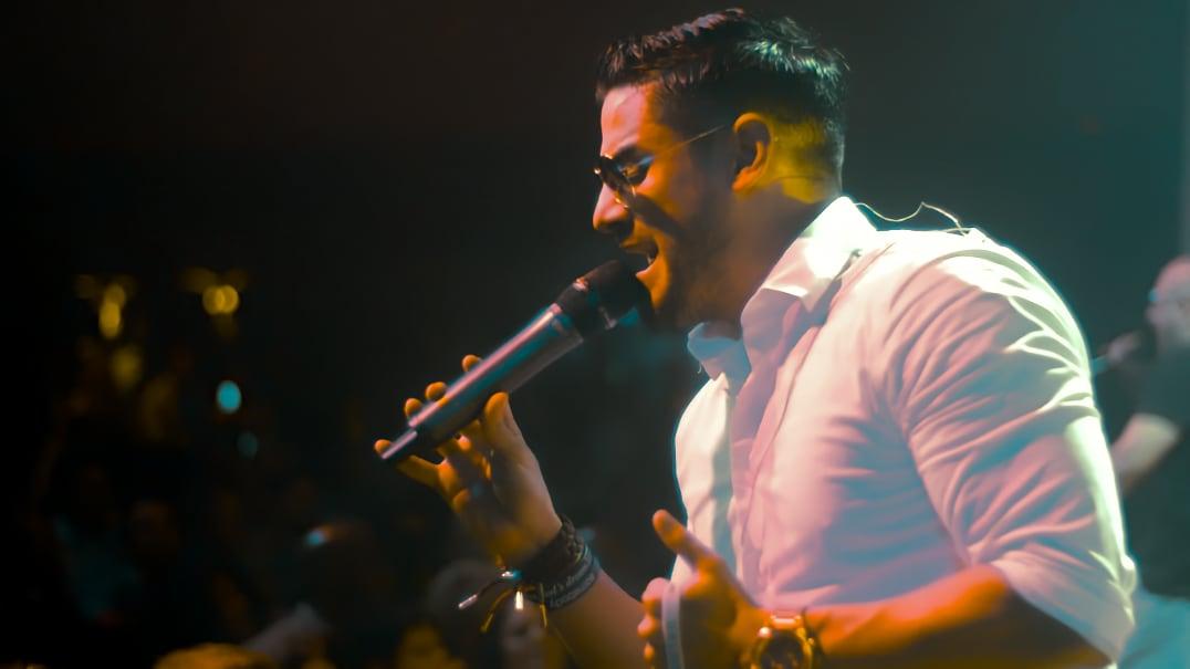 Man in a white shirt singing passionately into a microphone on stage.