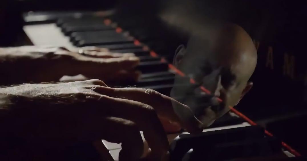 Hands playing piano keys with a man’s face reflected on the glossy surface.