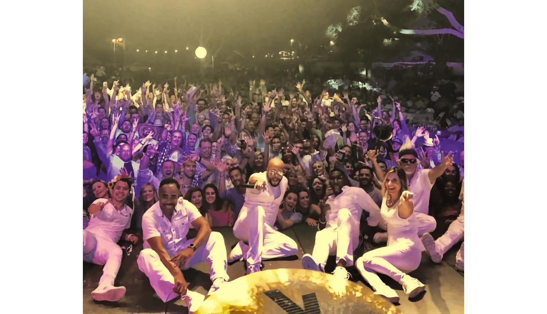 Performers in white pose on stage in front of a cheering crowd under purple lights.
