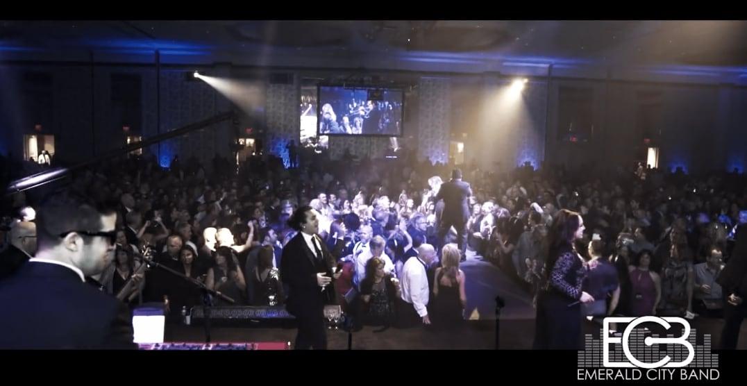 Large crowd at a formal event with a band performing on stage under blue and yellow lights.