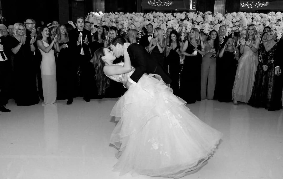 Bride and groom share a kiss on the dance floor surrounded by applauding guests.