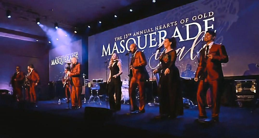 Band performing on stage under purple lighting at a masquerade gala event.