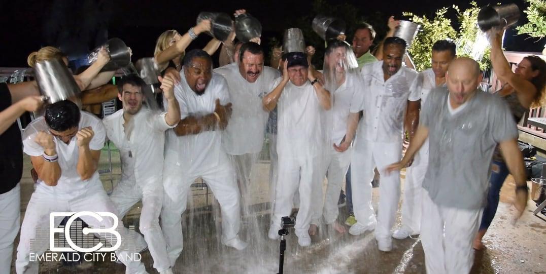 Group of people in white clothing doing the ice bucket challenge at night.