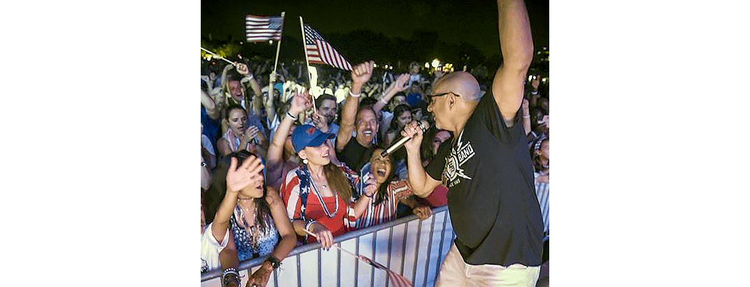 Singer performing on stage at night, hyped crowd reaching toward him.