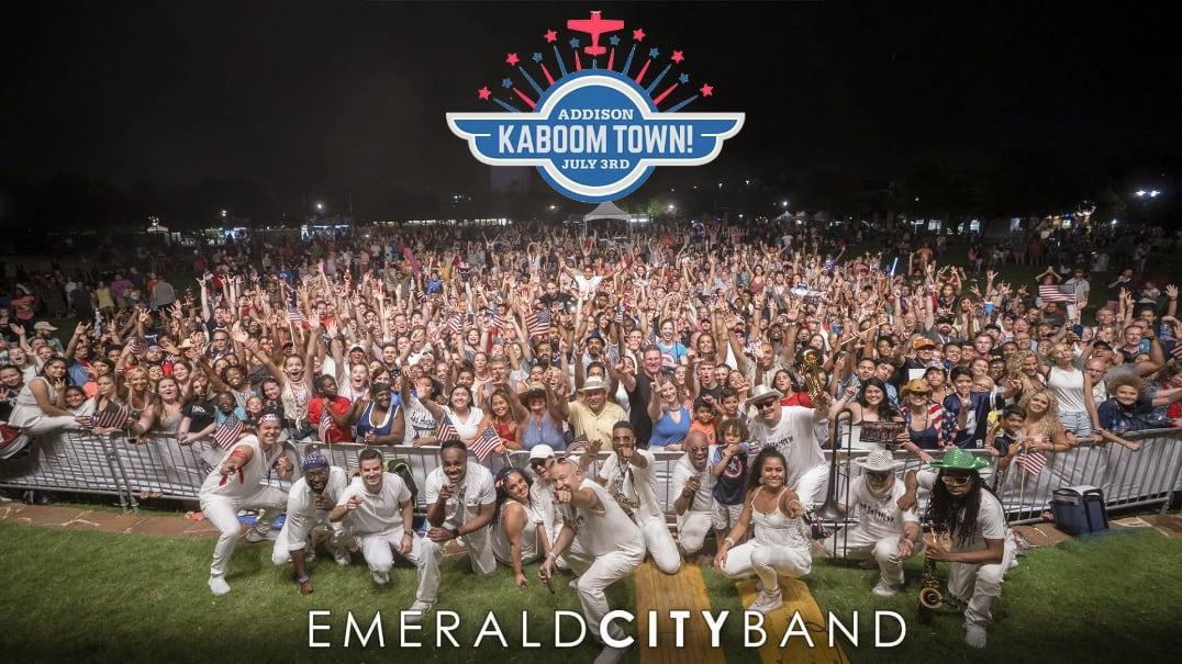 Emerald City Band posing in front of a large, cheering outdoor crowd at night.
