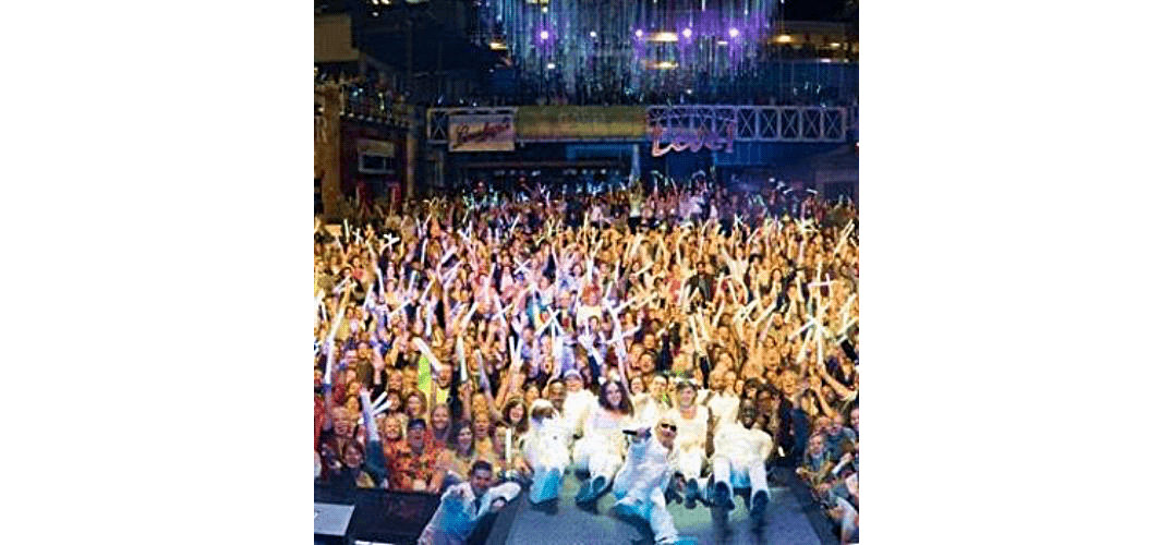 Large, cheering crowd at a nighttime outdoor concert with bright stage lights.
