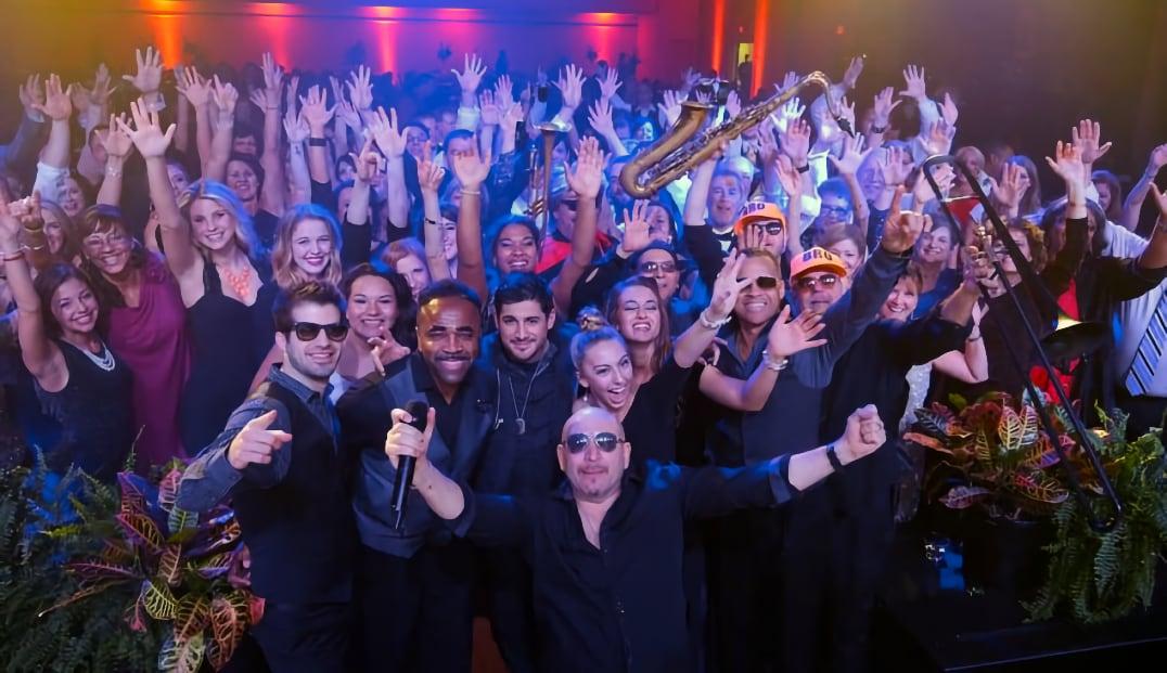 Large group of people at a lively party, smiling and raising their hands.