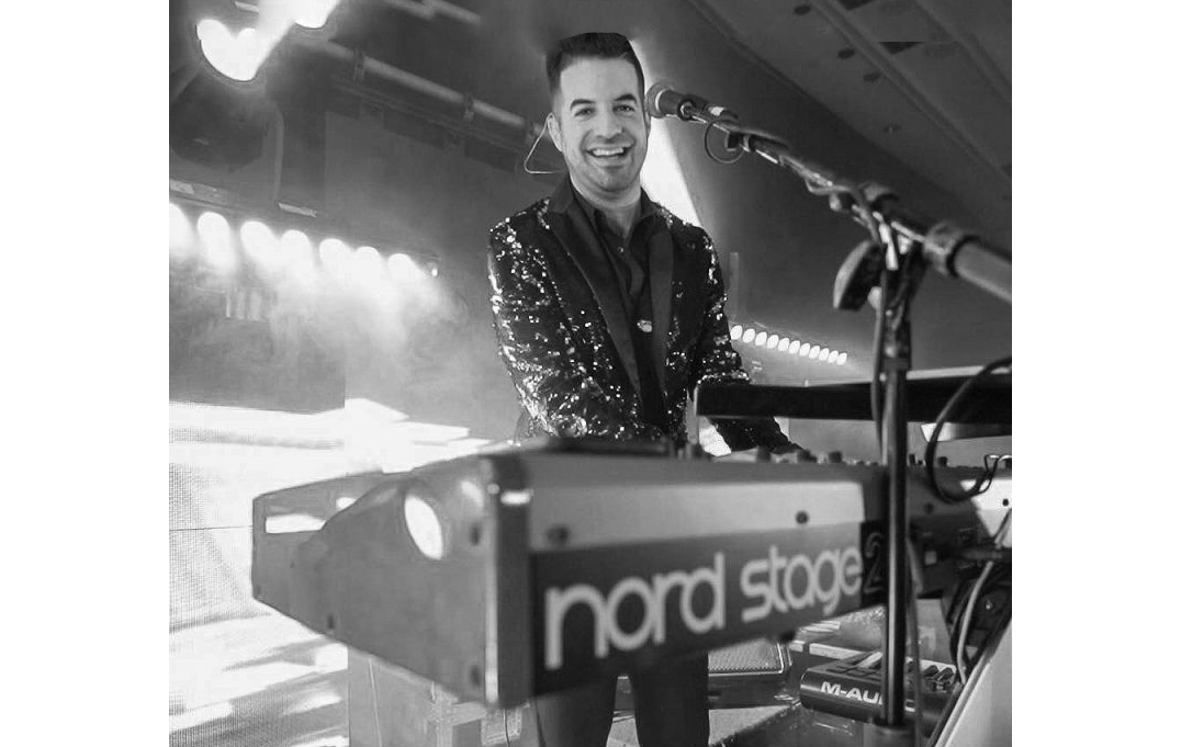 Smiling musician playing a Nord Stage keyboard on stage under bright lights.